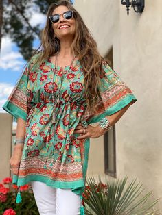 Our Fiji Floral short kaftan is named for Republic of Fiji with its beautiful white beaches and stunning tropical flowers. Jean Marie's beloved uncle Denny lived for 17 years in Fiji, after leaving India, and she recalls fondly his tales of this magical island which she still has yet to visit! This beautiful tropical floral print is hand block printed on lightweight cotton voile. It has a beautiful applied decorative border. It will bring you a little taste of paradise at any time of year. The drawstring tassels are hand beaded and swing gracefully as you stroll along spreading PAX! One size with adjustable drawstring waist Length 32" 100% Cotton lightweight voile Delicate machine wash cold in a lingerie bag to protect tassels or hand wash cold. Hang dry. Made in India This fabric is block Bohemian Short Sleeve Floral Print Tunic, Green Floral Print Vacation Tunic, Green Floral Print Tunic For Vacation, Green Bohemian Short Sleeve Kimono, Bohemian Tunic Kaftan For Holiday, Traditional Green Tunic For Vacation, Traditional Beach Tunic With Floral Print, Traditional Floral Print Beach Tunic, Short Kaftan