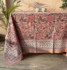 a table covered with a pink and blue floral print cloth next to potted plants