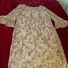 a white dress with gold sequins on it sitting on a red velvet bed