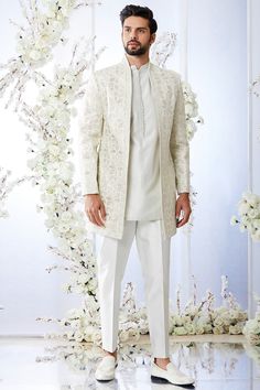 a man in a white outfit standing next to a floral wall with flowers on it