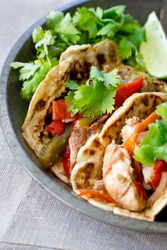 some tacos are sitting in a bowl with cilantro and lime wedges