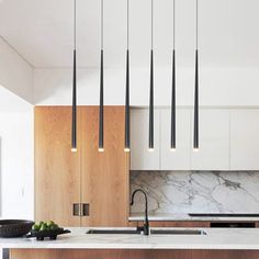 a kitchen with marble counter tops and hanging lights over the island, surrounded by wooden cabinets