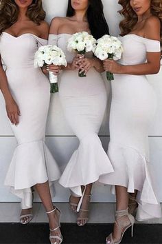 three women in white dresses standing next to each other holding bouquets and posing for the camera