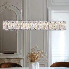 a chandelier hanging over a dining room table with flowers in the vase on it