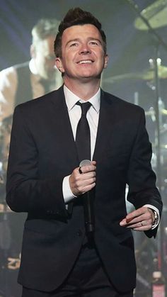 a man wearing a suit and tie holding a microphone in front of a band on stage