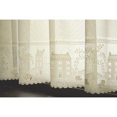 a window with white lace curtains and houses on the windowsill in front of it