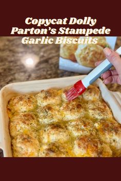 a person holding a paintbrush over a casserole dish with garlic bread in the background