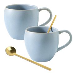 two blue mugs with gold handles and spoon next to each other on a white background