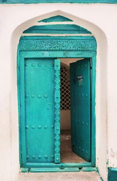 an open blue door on the side of a white and green building with intricate designs