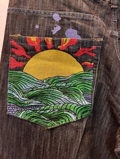 the back pocket of a pair of jeans with an embroidered sun and waves on it