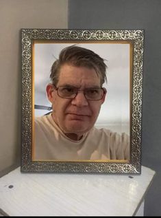 an old man with glasses is looking at the camera in front of a framed photo