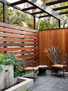 an outdoor patio with two chairs and a planter in the center, next to a wooden fence