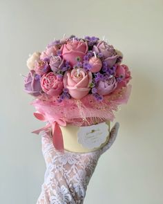 a woman's hand holding a pink and purple flower arrangement in a hat box