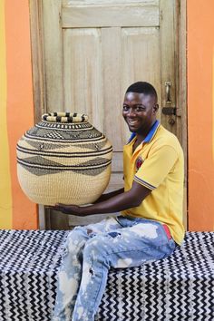 a young man sitting on a bench holding a basket in front of him and smiling at the camera