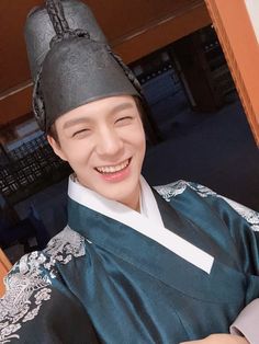 a young man wearing a black hat and green robe smiling at the camera with his eyes closed