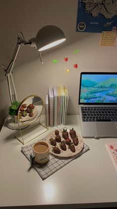 a laptop computer sitting on top of a desk next to a plate of food and cup