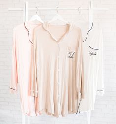 three women's shirts hanging up against a white brick wall, with the words good luck written on them