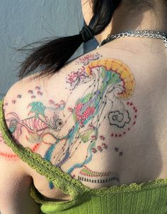 the back of a woman's shoulder with colorful tattoos on her arm and chest