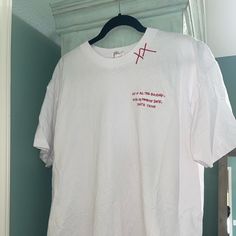 a white t - shirt with red writing on it hanging from a hanger in front of a door