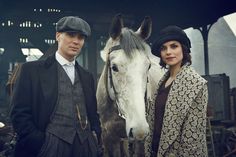 a man and woman standing next to a horse in front of a covered area with buildings