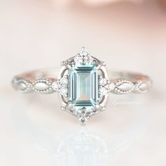 an emerald colored stone surrounded by white diamonds in a ring on top of a table