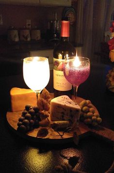 a wine glass and some cheese on a wooden board with candles in the background at night