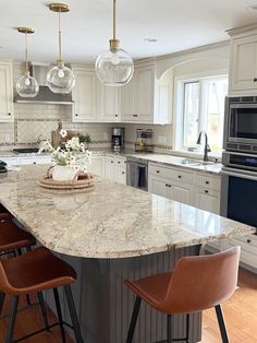 a large kitchen with marble counter tops and stools in front of an island that has three hanging lights above it