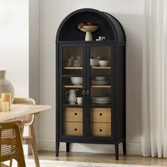 a black cabinet with glass doors and drawers next to a dining room table in front of a window