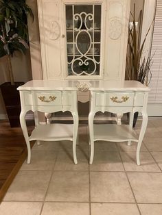 two white tables with gold trim on them in front of a door and potted plant