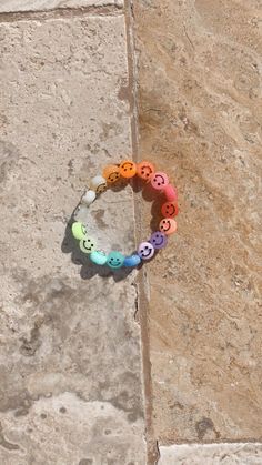 a multicolored beaded bracelet with smiley faces is sitting on a stone surface