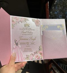 a person holding up a pink and gold wedding card