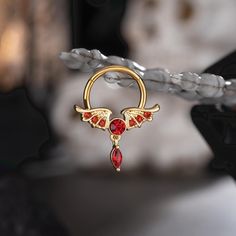 This wings shape red gems dangle septum ring design is so dainty. The three different choices bring out distinctive sensations due to the change of color and gem combinations.The gold one exudes royal elegance. The black one with red CZ gems encapsulates an air of mystery and intrigue. The steel one offers a sense of purity and divine spirit. You can easily pick which one suits you the best, or take them all for a change of looks and moods. Dainty Septum Ring, Dainty Septum, Titanium Belly Button Rings, Divine Spirit, Red Gems, Ring Day, Conch Hoop, Dangle Belly Rings, Dragon Claw