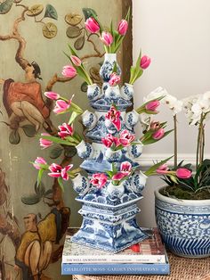 two blue and white vases with pink flowers in them on a table next to books