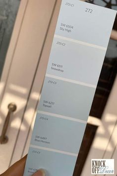 a person holding up a white paint swatch in front of a door with the words sky blue on it