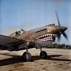 an old airplane with a shark's mouth painted on the side and two people sitting in it