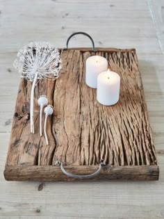 a wooden tray with two white candles and some dandelions