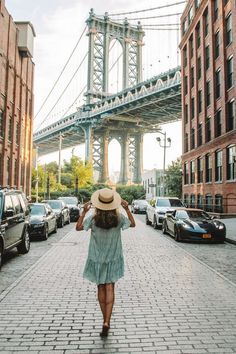 a woman walking down a brick street in front of a bridge and cars on the road