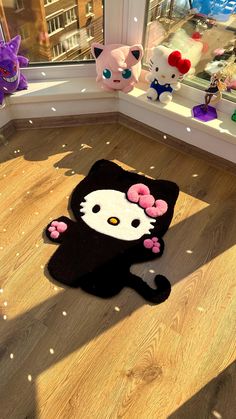 a hello kitty rug on the floor in front of a window with other stuffed animals