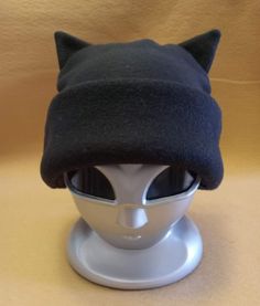 These super fun, unique and soft, fleece Cat Ear Hats are great fun to give and wear! They are all created and handmade by Groovy Moods. Each hat will have your choice of a black, white or grey body with the band and ears available in red, pink, orange, yellow, green, blue, purple, black, white or grey. Great for cat lovers everywhere!  One Size fits child to adult ~ not intended for infants Secondary color shades may vary slightly. Adjustable Beanie Hat For Cosplay, Black Cosplay Hat, One Size Fits Most, Black Hat For Cosplay, One Size Fits Most, Adjustable Beanie For Cosplay, Black Cosplay Hat One Size Fits Most, Black Cat Ears Hat With Cat Design, Adjustable Cat Ears Winter Hat, Adjustable Cat Ears Beanie For Winter, Adjustable Warm Hat With Cat Ears