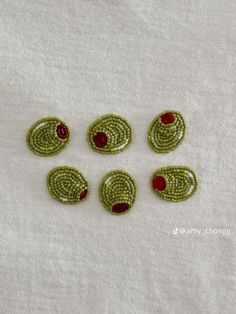 six green and red beaded buttons on a white cloth