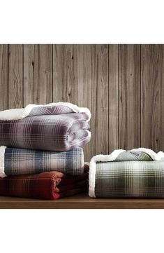 three blankets stacked on top of each other in front of wooden wall with planks