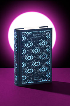 a book sitting on top of a purple table next to a full moon with an eye pattern