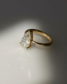 a yellow gold ring with a pear shaped diamond in the center, on a white surface