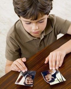 a young boy sitting at a table with two pictures on the table and one is holding his hand