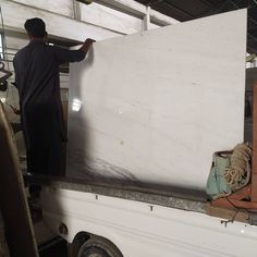 a man standing on the back of a white truck in a garage next to a pile of wood