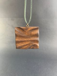 a wooden square pendant hanging from a green cord on a gray surface with a white background