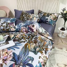 a bed covered in lots of colorful flowers on top of a wooden floor next to a white headboard