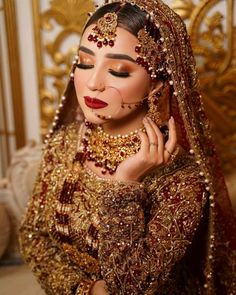 a woman wearing a gold and red bridal outfit with her hands on her face