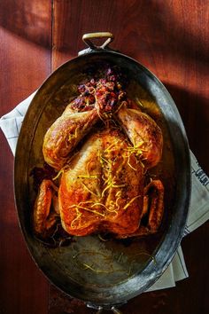 a roasted chicken in a pan on top of a wooden table next to napkins