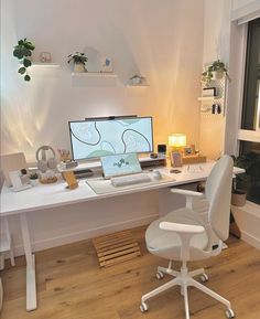 a white desk with a computer on it in front of a window and potted plants